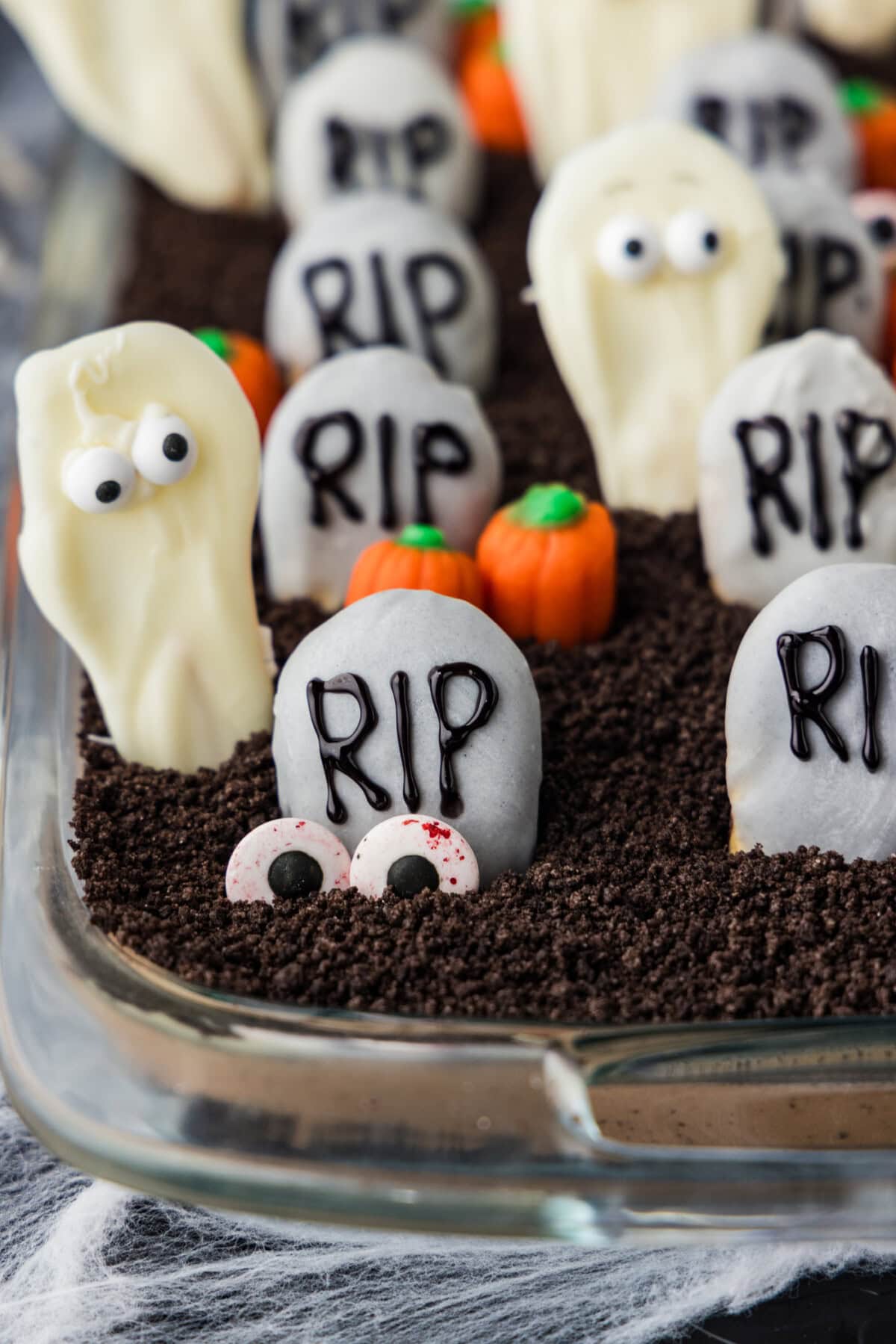 Halloween dirt cake topped with RIP cookie tombstones, white chocolate ghosts, candy pumpkins and candy eyeballs