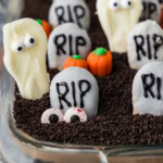 Halloween dirt cake topped with RIP cookie tombstones, white chocolate ghosts, candy pumpkins and candy eyeballs