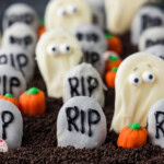 A cookie tombstone marked RIP standing in Oreo crumb dirt beside a white chocolate ghost
