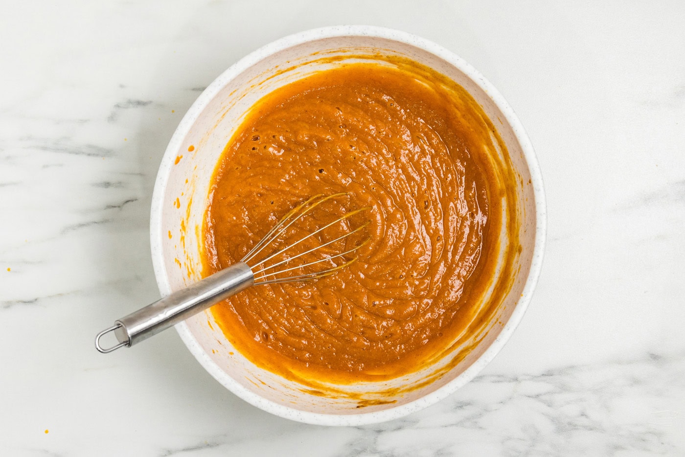 Canned pumpkin pie mix whisked smooth with eggs in a white bowl