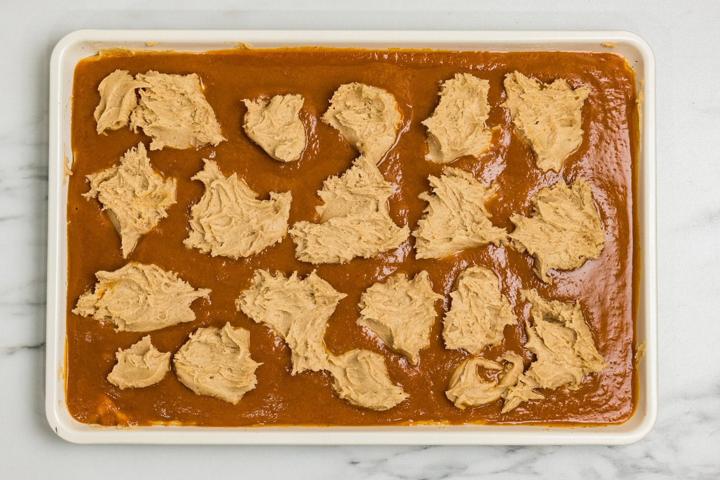 Spoonfuls of cake batter dropped over the pumpkin filling with gaps left between them