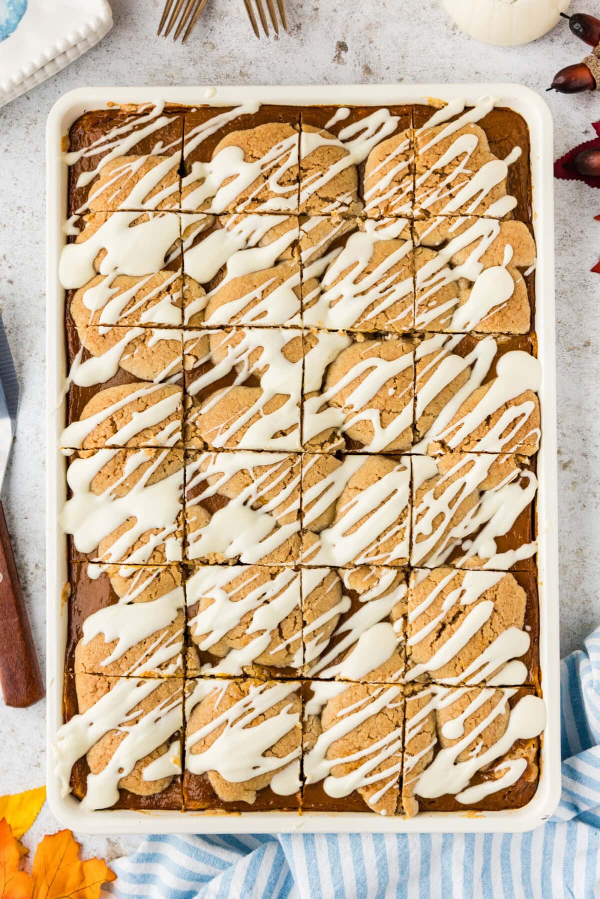 Overhead of pumpkin pie squares cut into 24 pieces in a white jelly roll pan with cream cheese drizzle