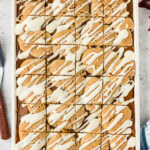 Overhead of pumpkin pie squares cut into 24 pieces in a white jelly roll pan with cream cheese drizzle