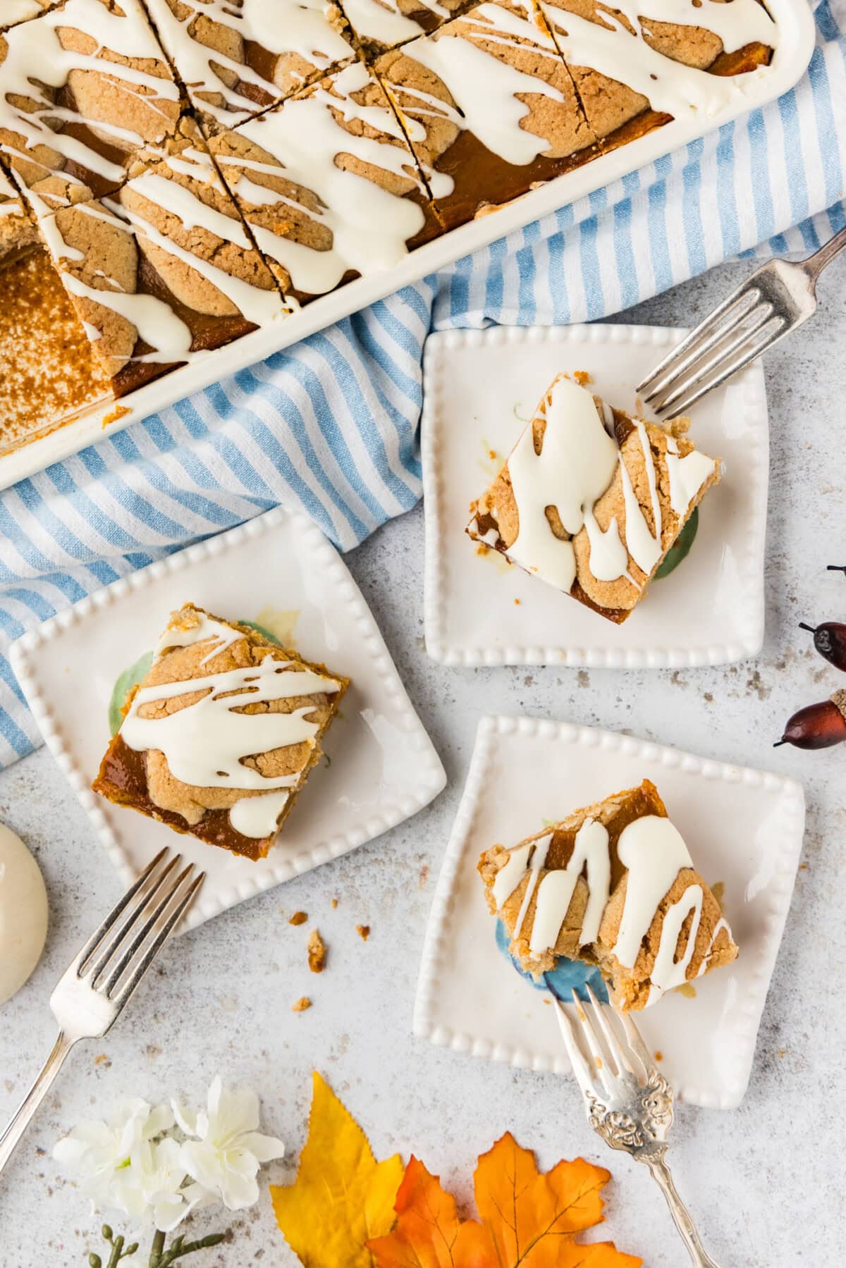 Pumpkin pie squares served on small white plates beside the baking pan with forks and fall leaves