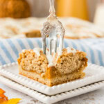 A fork pressing into a pumpkin pie square on a white scalloped plate