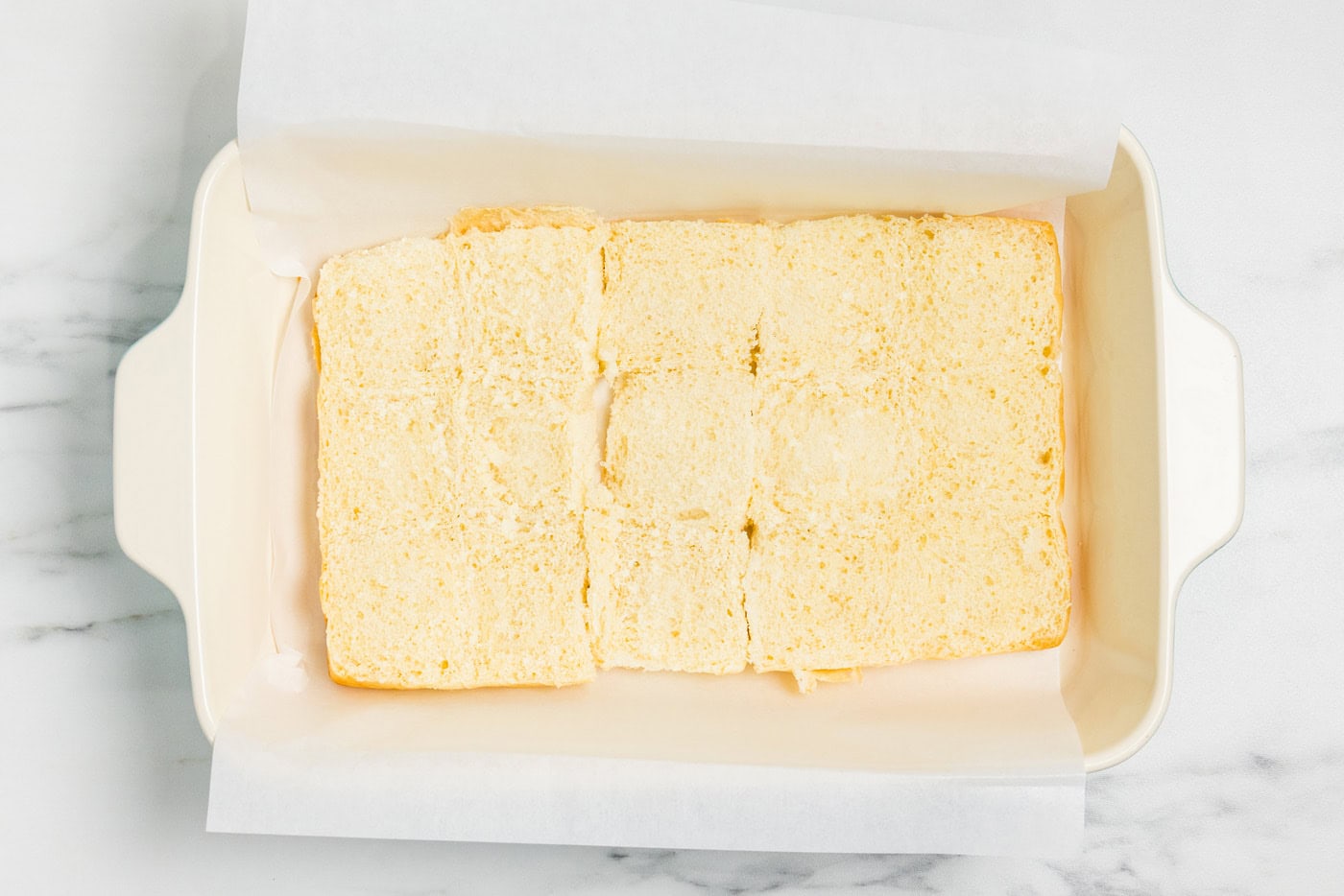Bottom halves of Hawaiian rolls cut side up in a parchment lined 13x9 baking dish