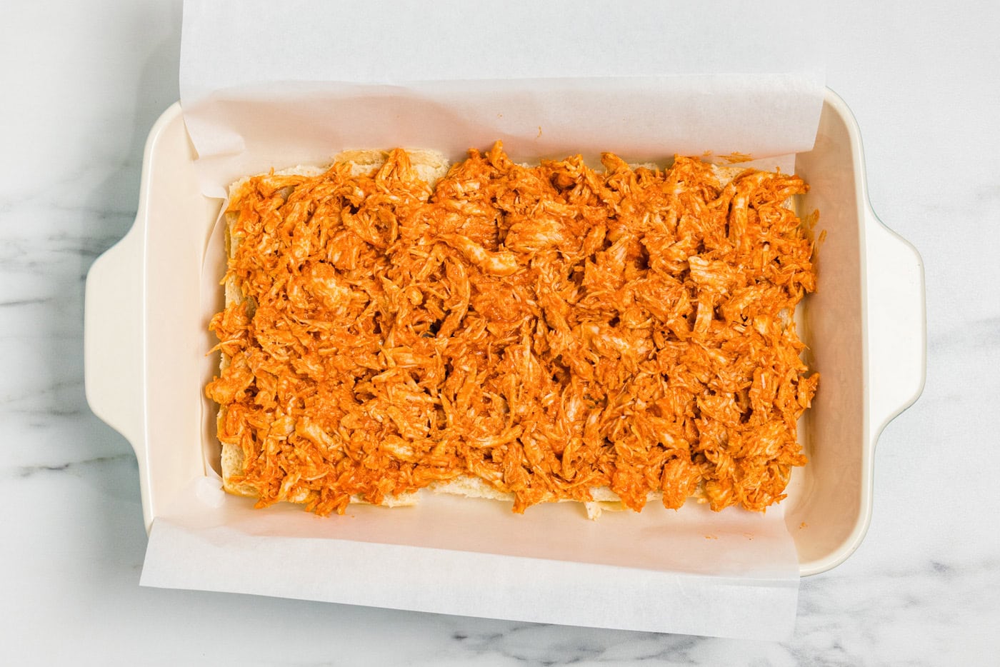 Buffalo chicken spread in an even layer over the bottom buns in a baking dish