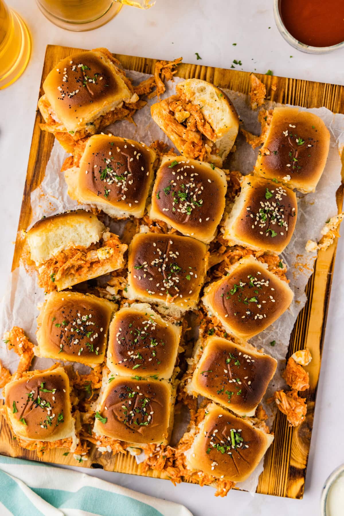 Overhead of buffalo chicken sliders with seeded tops on a wooden board with hot sauce and blue cheese dressing on the side