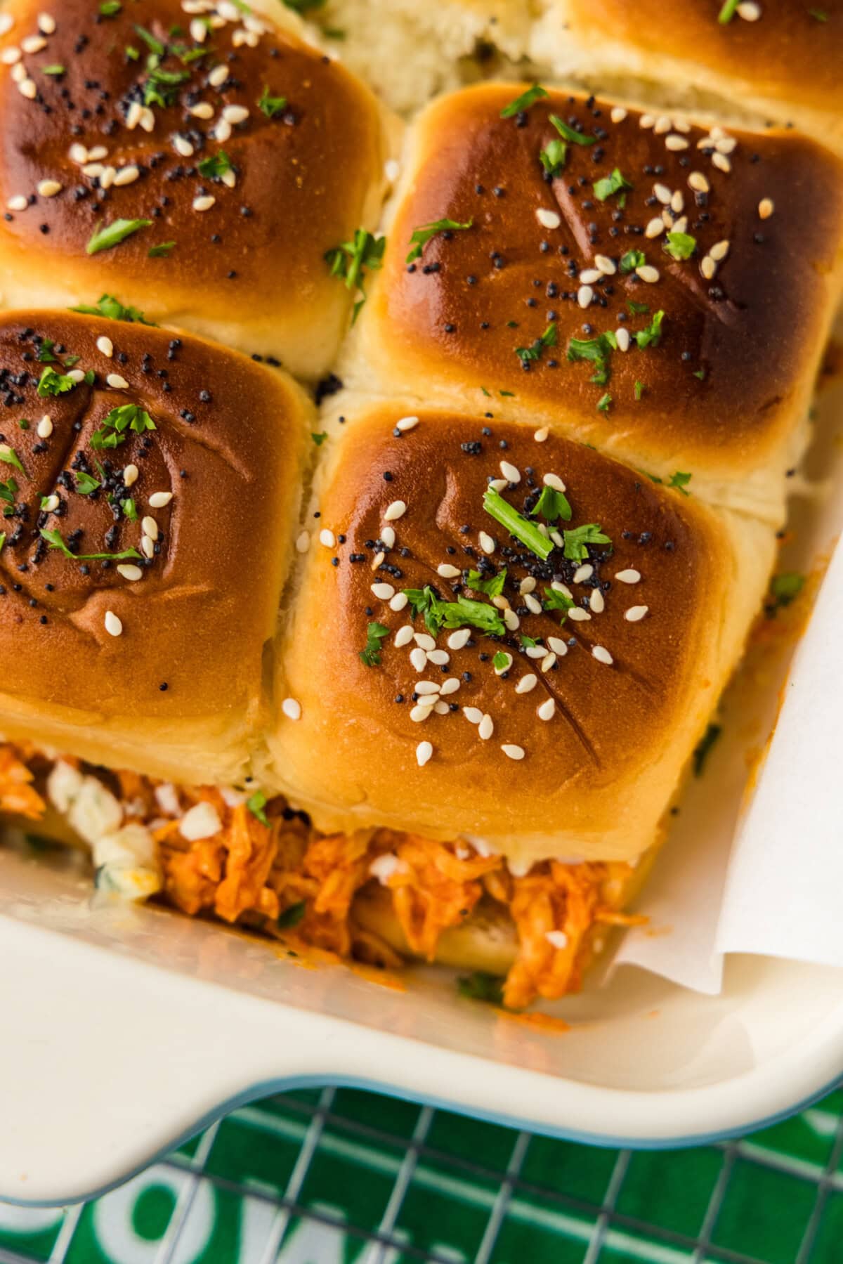 Close up of golden Hawaiian roll tops with sesame seeds, poppy seeds and parsley over buffalo chicken