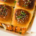 Close up of golden Hawaiian roll tops with sesame seeds, poppy seeds and parsley over buffalo chicken