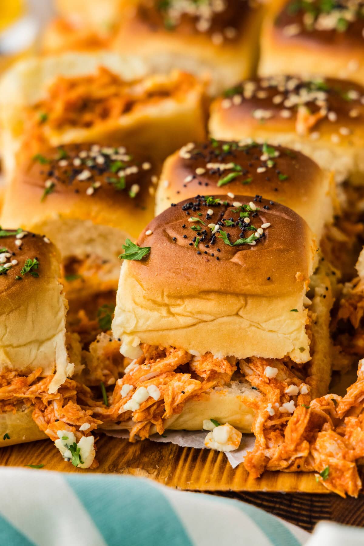 Buffalo chicken slider with shredded chicken and blue cheese crumbles spilling onto a wooden board