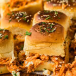 Buffalo chicken slider with shredded chicken and blue cheese crumbles spilling onto a wooden board