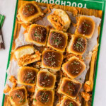 Overhead of buffalo chicken sliders on a wooden board set on a green touchdown football towel for game day