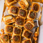 Overhead of buffalo chicken sliders on a wooden board with a serving spatula, hot sauce and blue cheese dressing