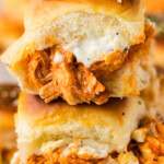 Close up of stacked buffalo chicken sliders with creamy blue cheese dressing over spicy shredded chicken