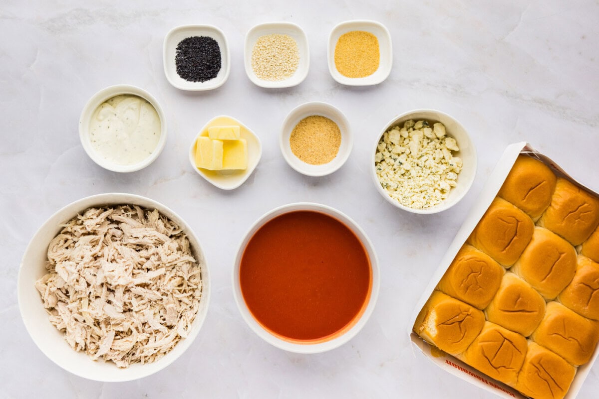 Ingredients for buffalo chicken sliders: shredded chicken, hot sauce, Hawaiian rolls, blue cheese crumbles, blue cheese dressing, butter, garlic powder, onion powder, poppy seeds and sesame seeds