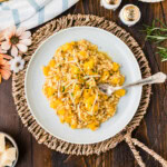 Overhead view of butternut squash risotto on a plate with fresh rosemary, Parmesan, and salt and pepper shakers.