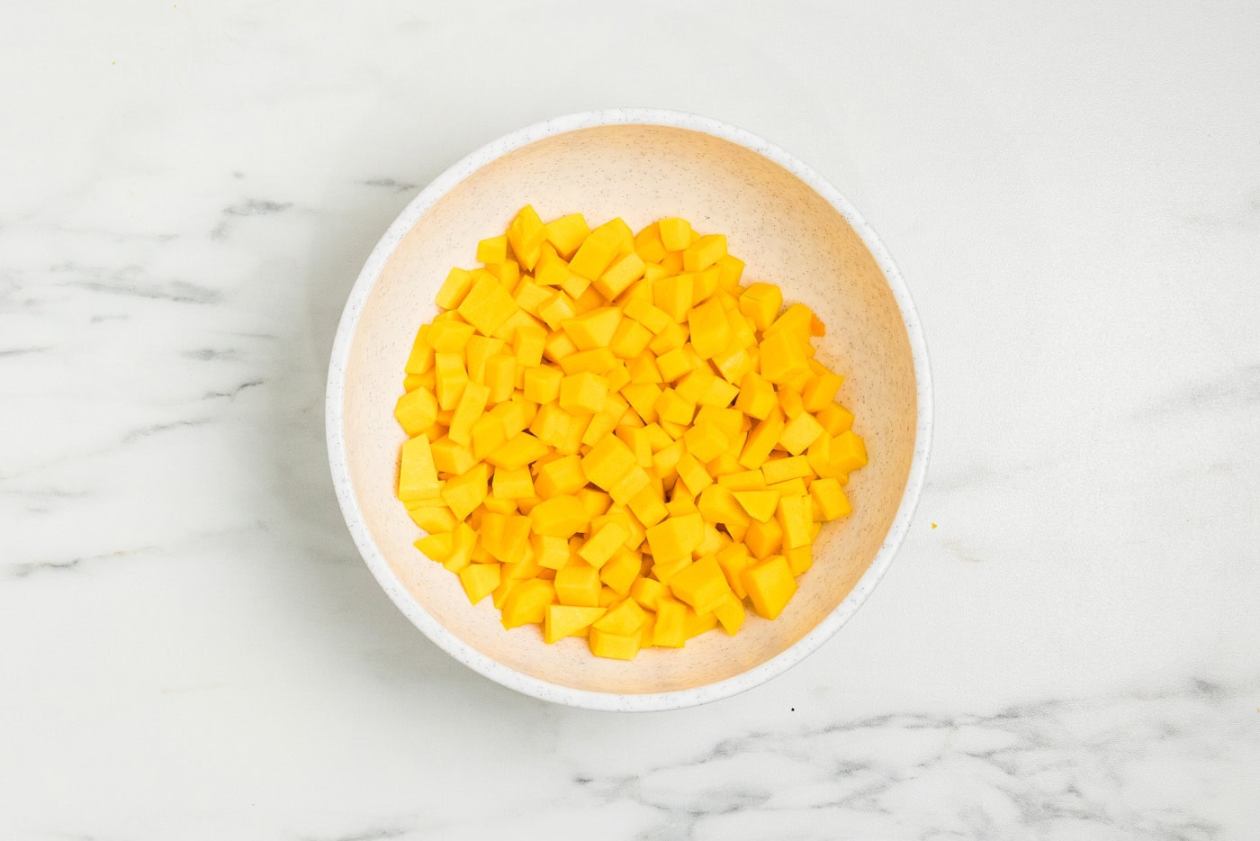 Peeled butternut squash cut into 1/2-inch cubes in a white bowl.
