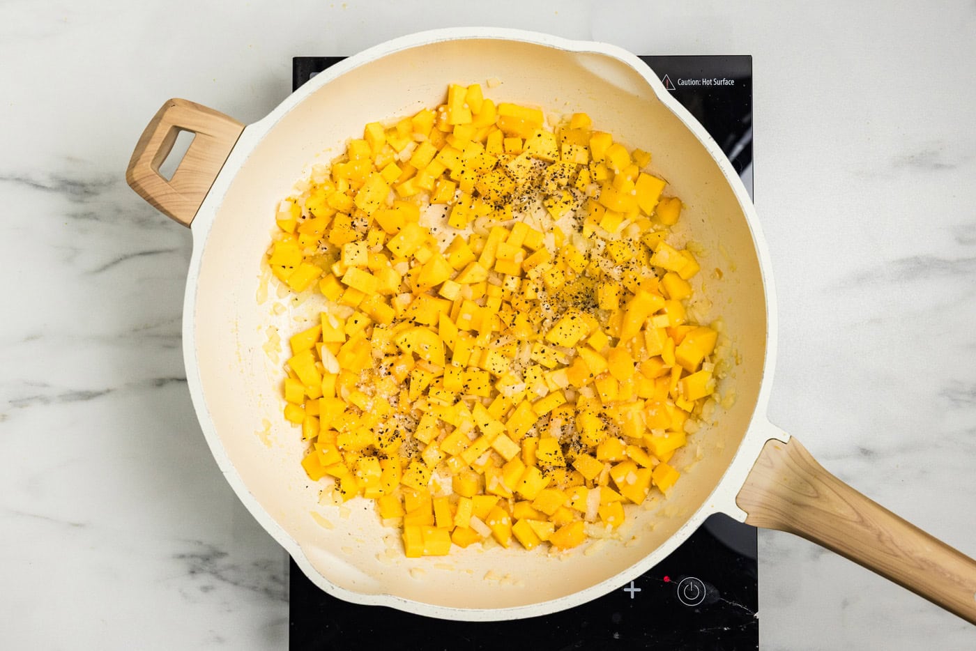 Butternut squash cubes and onion seasoned with black pepper and garlic salt in the skillet.