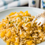 Close-up of creamy butternut squash risotto with shredded Parmesan and a fork on a plate.