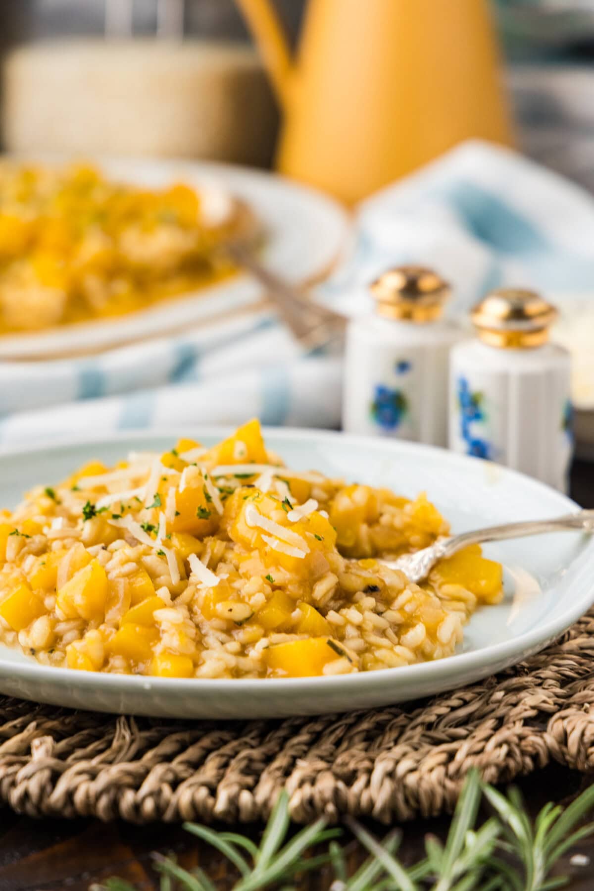 A plate of butternut squash risotto on a woven placemat with the serving platter in the background.