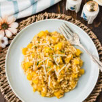 Overhead view of butternut squash risotto on a plate with shredded Parmesan, parsley, and a fork.