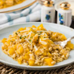 A serving of butternut squash risotto with tender squash cubes and shredded Parmesan on a woven placemat.