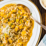 Butternut squash risotto on a serving platter with a spoon, garnished with grated Parmesan and parsley.