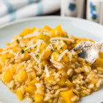 Close-up of a plate of creamy butternut squash risotto with shredded Parmesan and a fork.