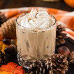 A pumpkin spice mudslide topped with whipped cream and spice, surrounded by pinecones and acorns