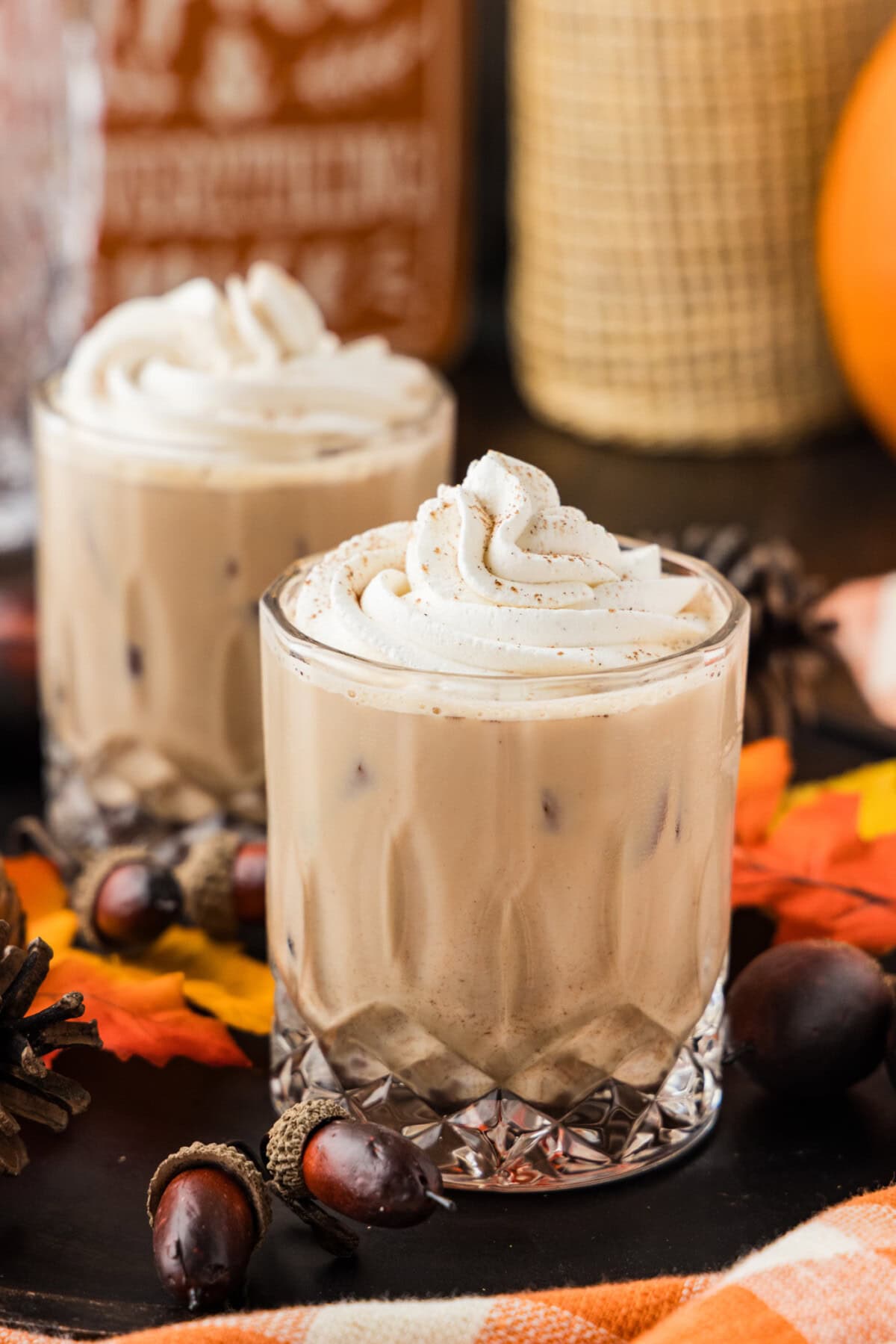 Two pumpkin spice mudslides topped with whipped cream and a dusting of spice beside a pumpkin and fall leaves