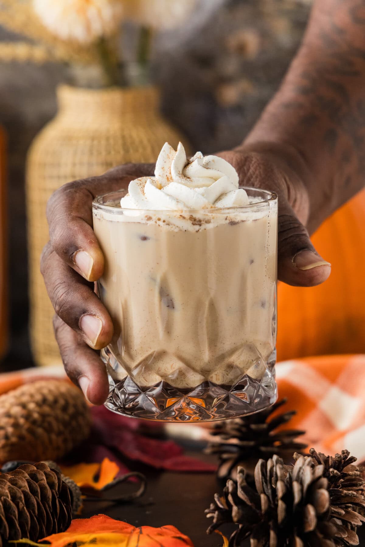 A hand holding a glass of pumpkin spice mudslide in front of a pumpkin and dried flowers