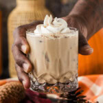 A hand holding a glass of pumpkin spice mudslide in front of a pumpkin and dried flowers