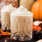 Two mudslides topped with whipped cream on a dark board with a pumpkin, acorns and an orange plaid cloth
