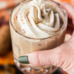 A hand holding a mudslide topped with whipped cream and a heavy dusting of pumpkin pie spice