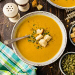 Roasted pumpkin soup in a stoneware bowl topped with croutons, pepitas and parsley.