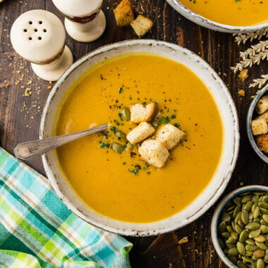 Roasted pumpkin soup in a stoneware bowl topped with croutons, pepitas and parsley.