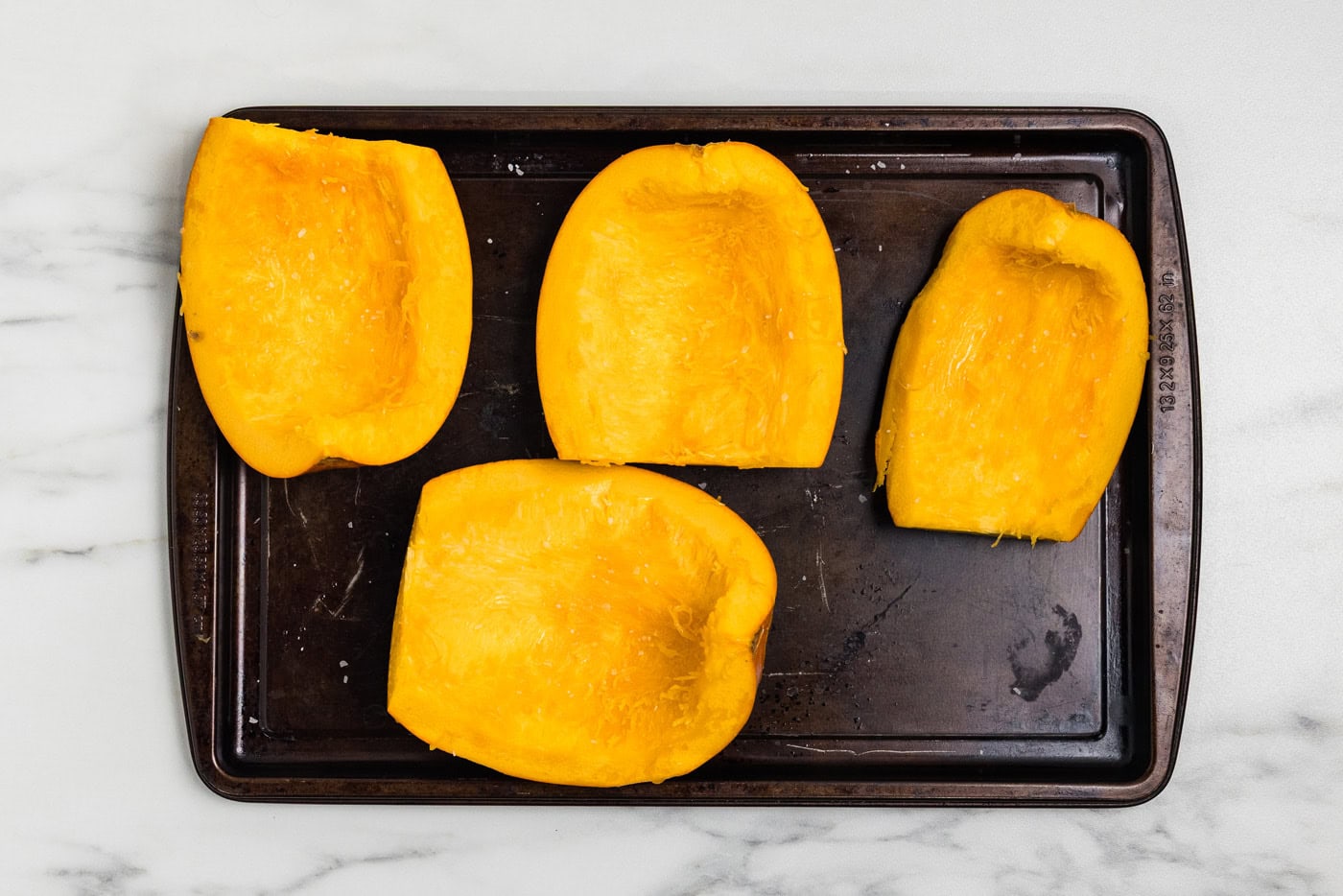 Sugar pumpkin quarters with the seeds removed, placed flesh side up on a baking sheet before roasting.