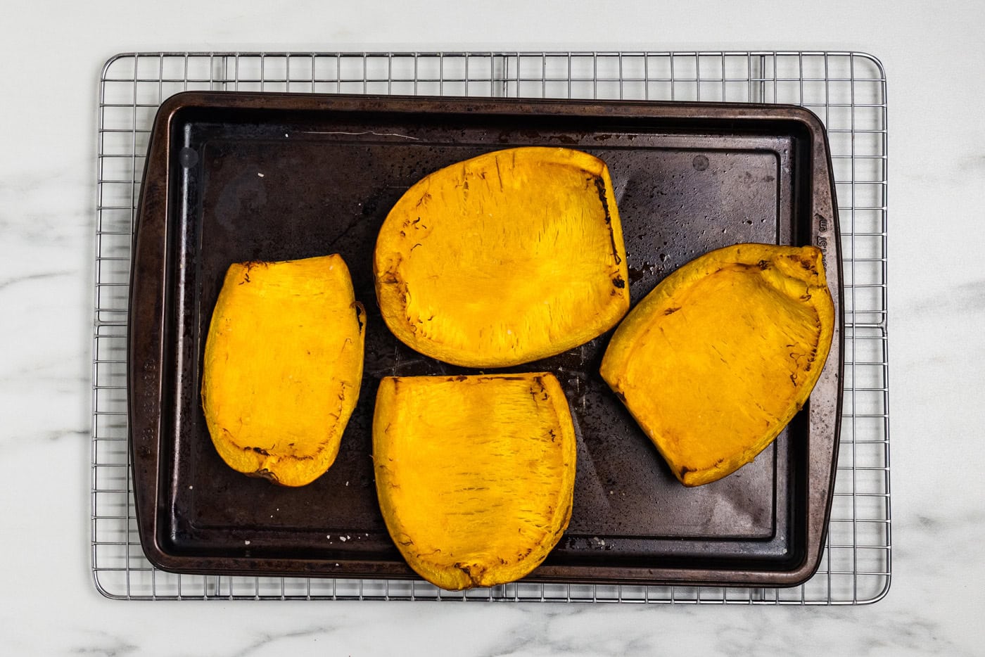Roasted sugar pumpkin quarters on a baking sheet cooling on a wire rack.
