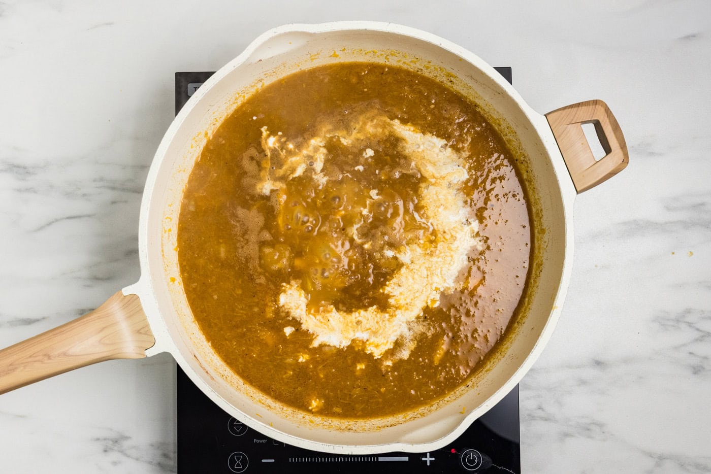 Heavy cream and maple syrup added to the pumpkin and broth mixture in a skillet.