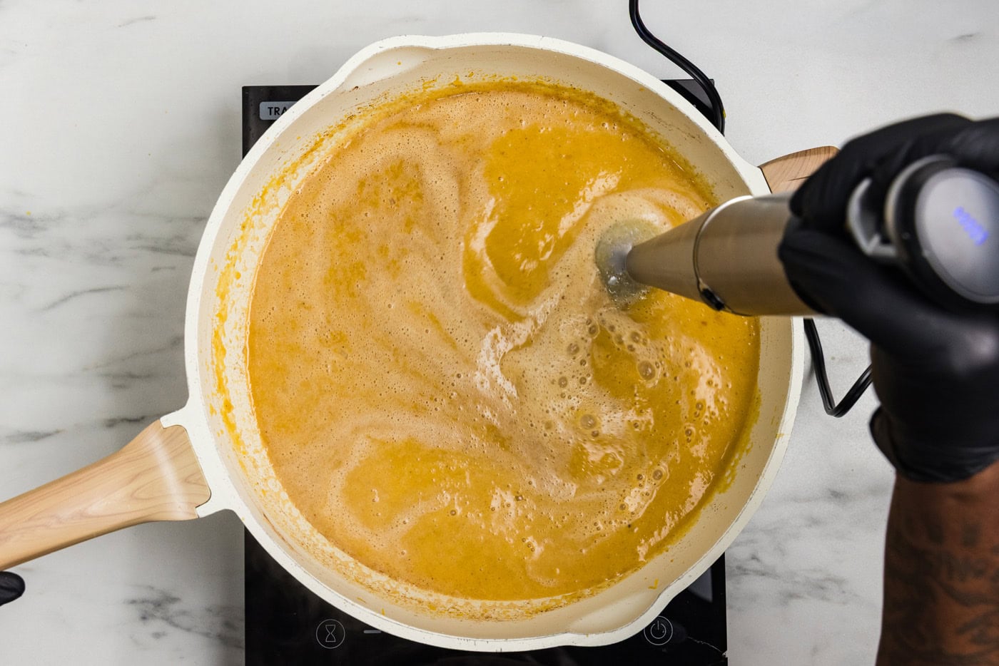 Immersion blender pureeing roasted pumpkin soup until smooth and creamy in a skillet.