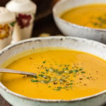 Side view of a bowl of creamy roasted pumpkin soup garnished with pepitas, parsley and black pepper.