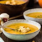 Bowl of roasted pumpkin soup topped with homemade croutons, with a second bowl of soup in the background.